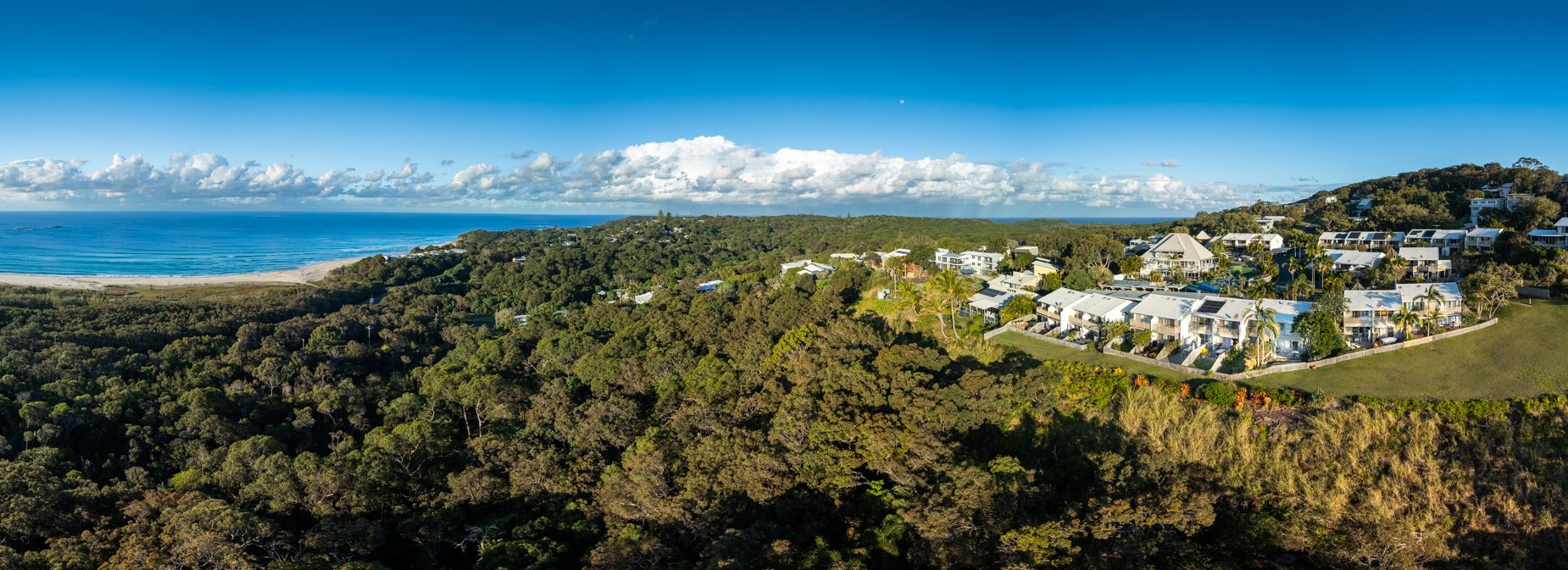 Coastal bushland running down to the beach and the ocean, with Pandanus Palms Resort and its headland reserve lawn on the right