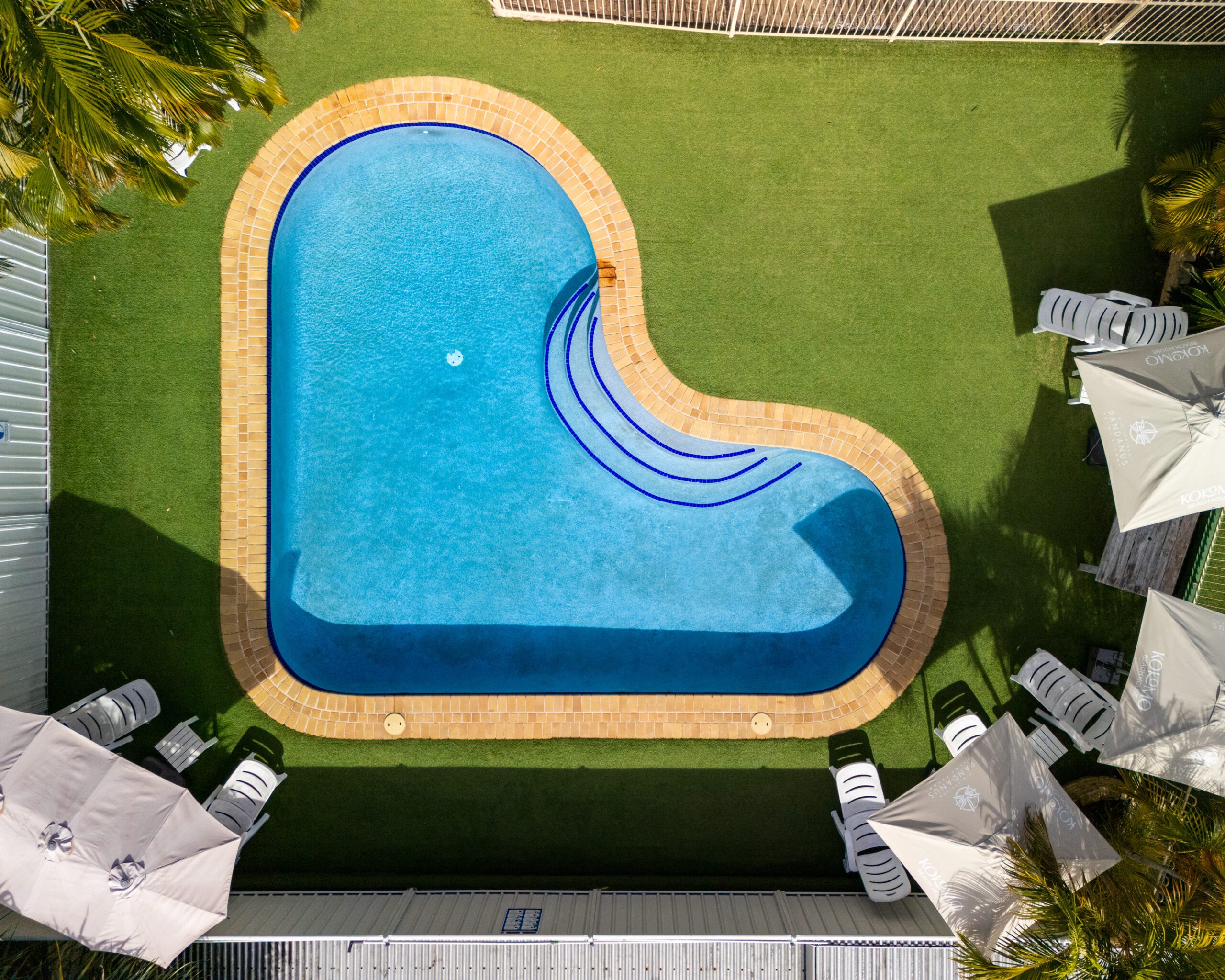 Overhead view of the swimming pool at Pandanus Palms Resort, edged with lawn and sun umbrellas