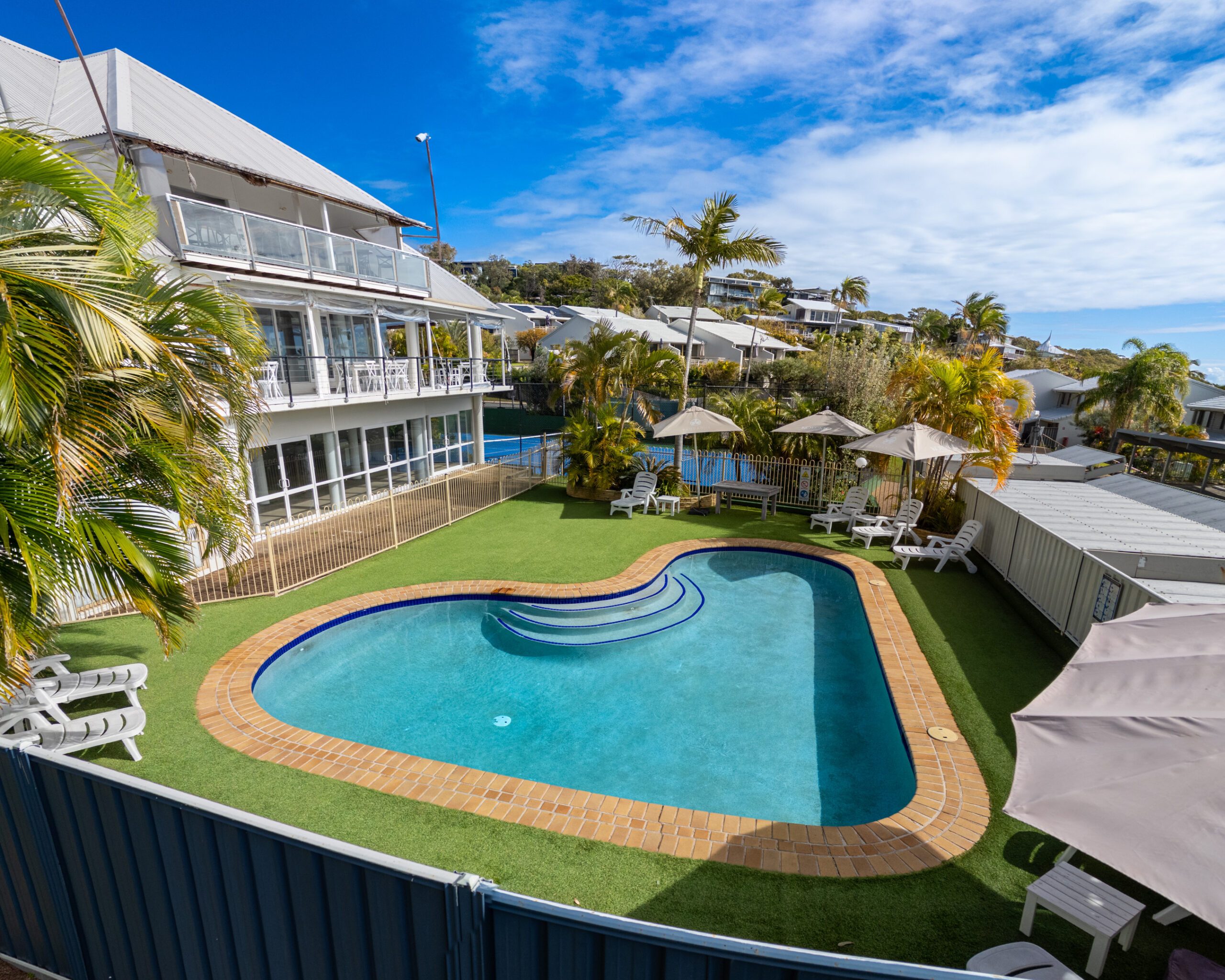 The swimming pool at Pandanus Palms Resort with sun lounges on the lawn and villas behind