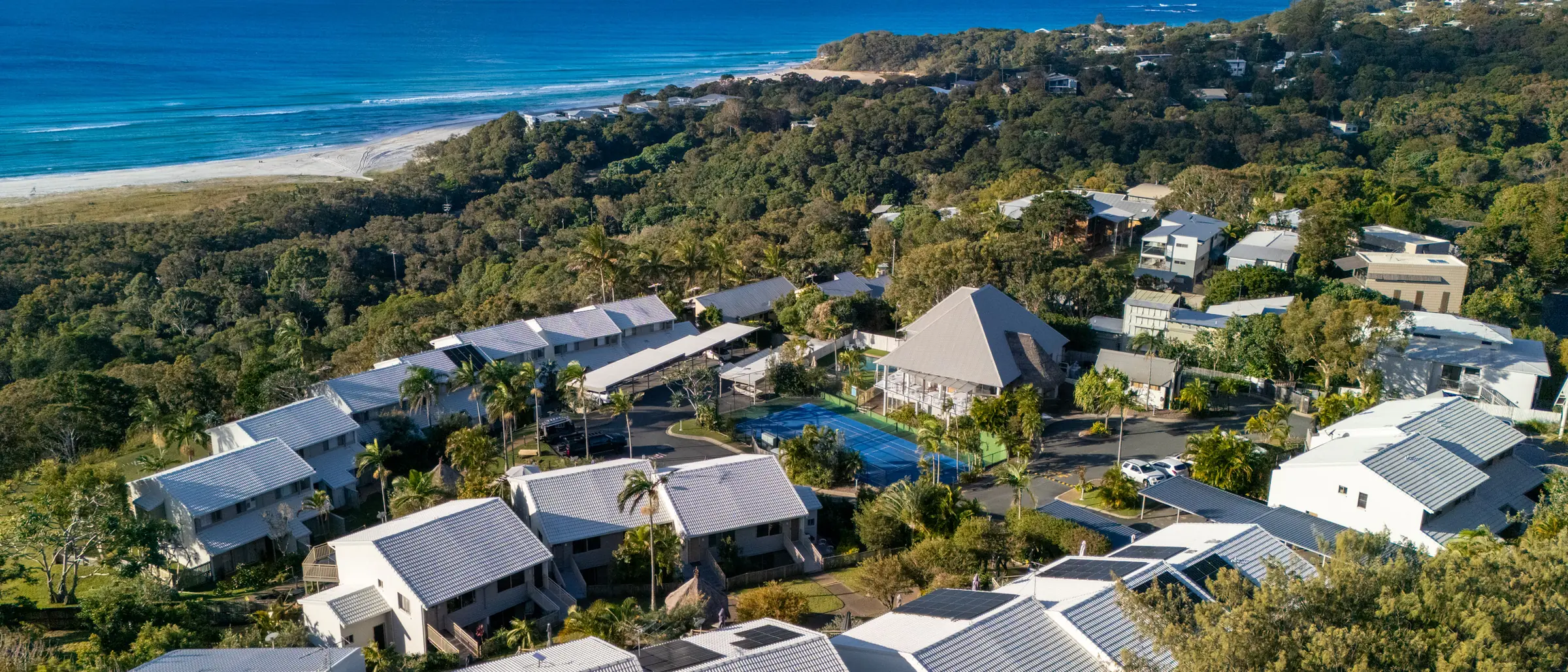 The headland at Pandanus Palms Resort from the air, with the villas among the trees and the beach and the Coral Sea beyond