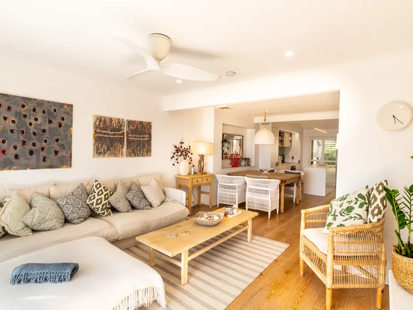 A bright villa living room with a white ceiling fan above a deep sofa and cane armchair