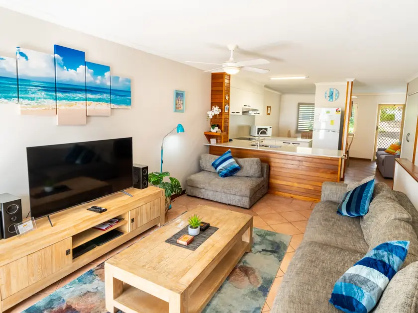 A villa living room with a large smart TV, sofas and the kitchen behind