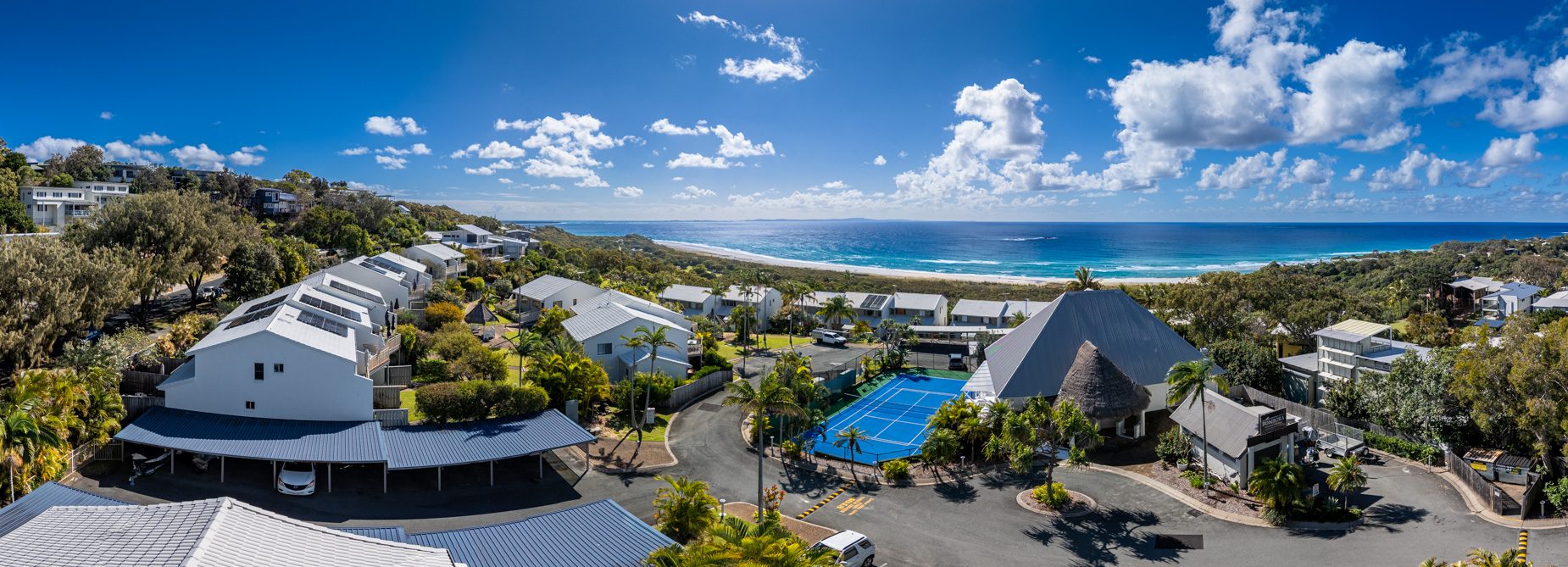 Panorama over the villas and the tennis court at Pandanus Palms Resort, with the beach and the ocean beyond