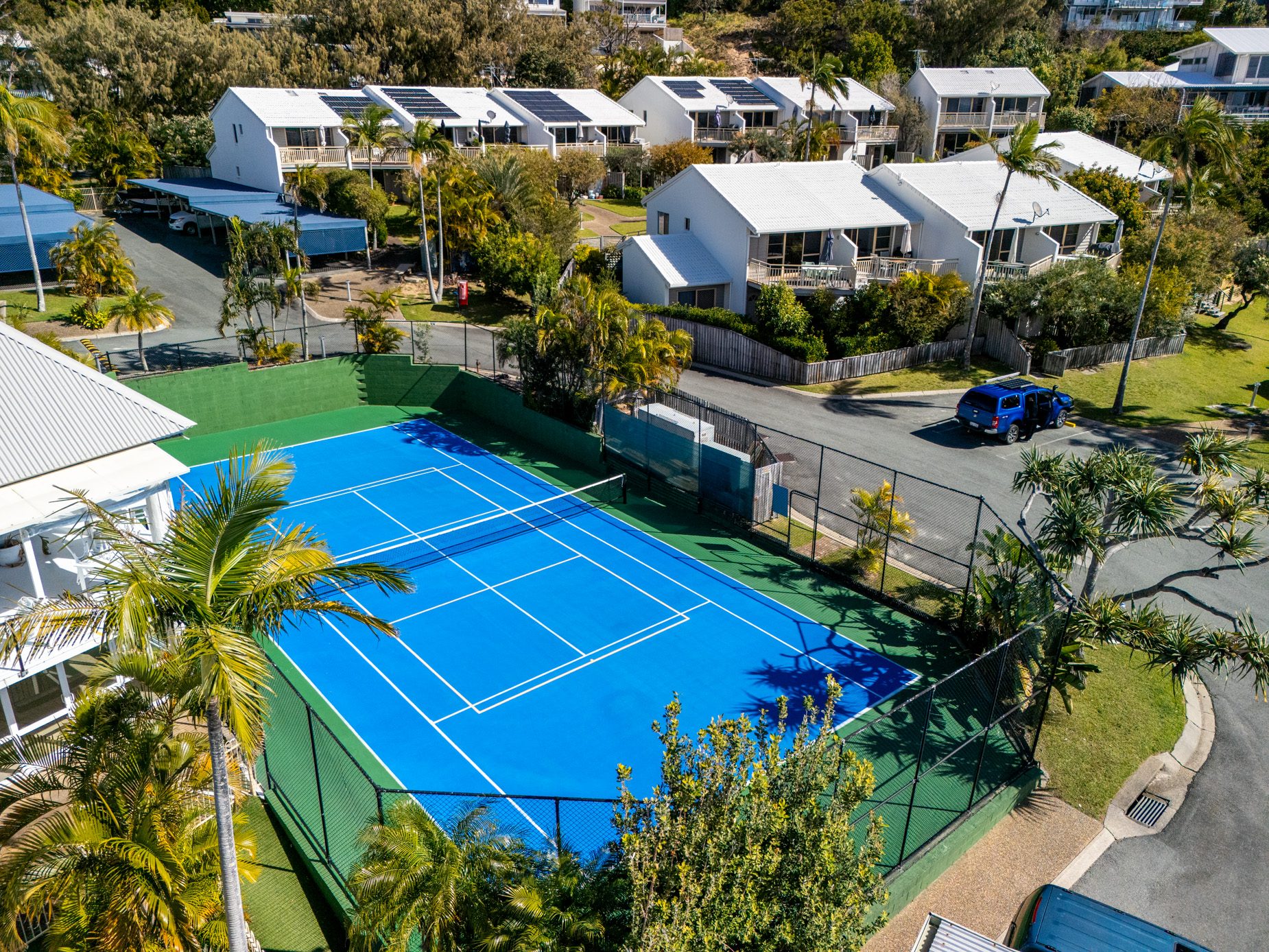 The blue tennis and pickle ball court at Pandanus Palms Resort, edged with palms, with two storey villas behind