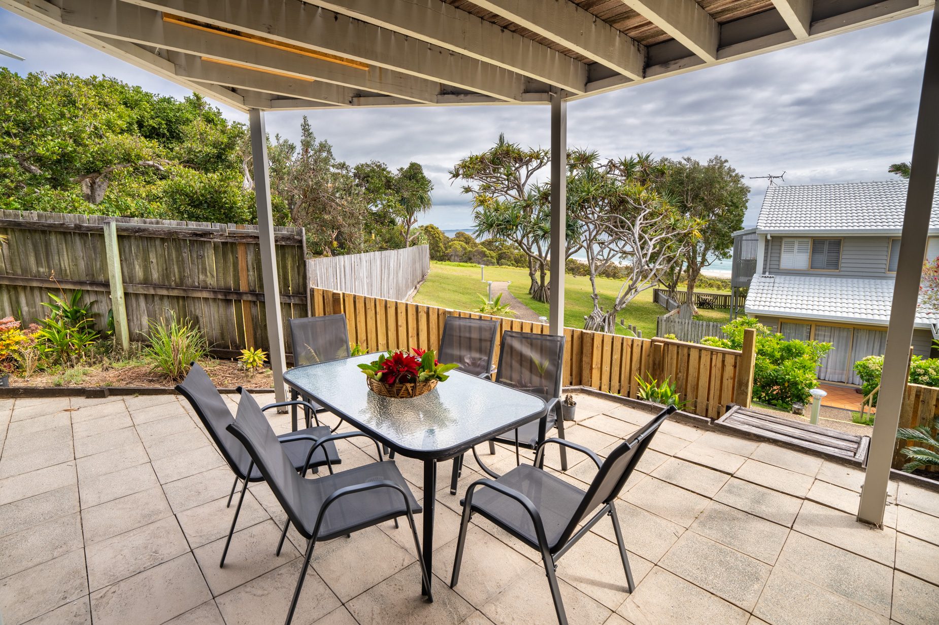 The paved courtyard with outdoor dining, looking across the lawn to the ocean from the Standard Headland Ocean 3 Bedroom villa