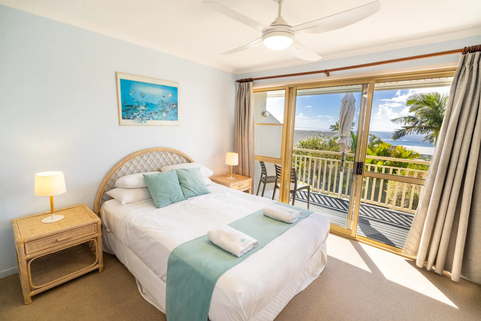 A bed made up with fresh white linen and towels in a villa bedroom, with the balcony and the ocean beyond